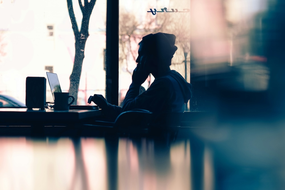 silhouette of a guy using a computer in a coffeeshop