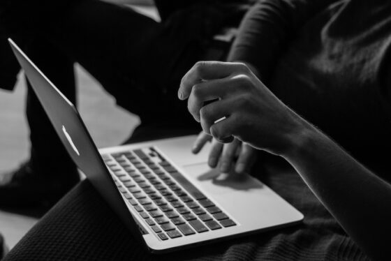 A black and white photo of a close up shot of a man's laptop being used.